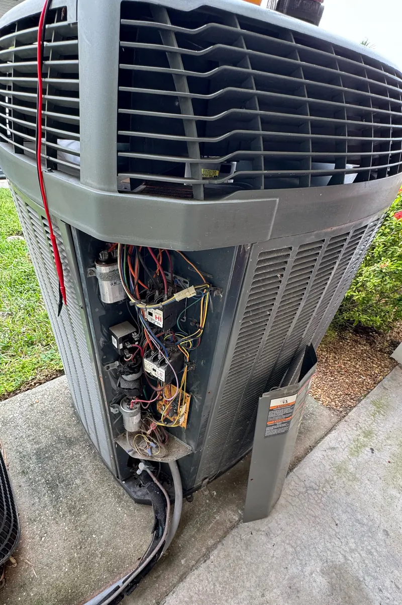 Outdoor condenser with the service panel removed and meter leads on the controls during a diagnostic