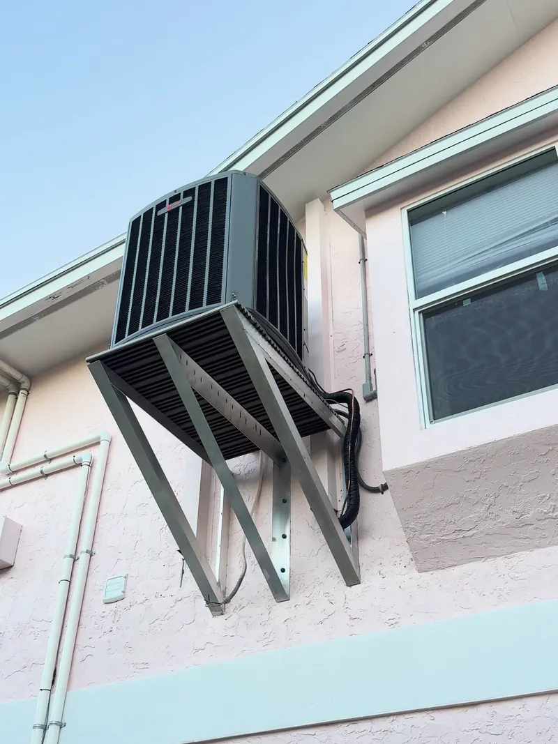 New condenser mounted on a wall bracket high on the side of a two-story stucco home