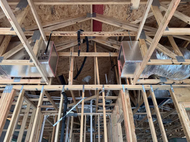 Insulated supply plenums and flex ductwork run through roof trusses in a new-construction home before drywall