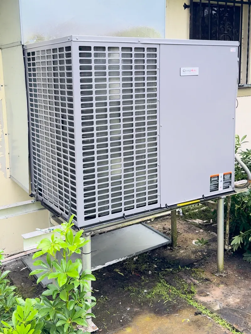 Packaged AC unit set on a raised metal stand beside a home, with a new sheet-metal duct transition